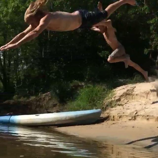 Two paddlers leaping off a sandy swamp bank into the water beside a kayak on a Honey Island tour